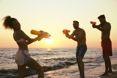 Photo of Friends with water guns having fun on beach at sunset