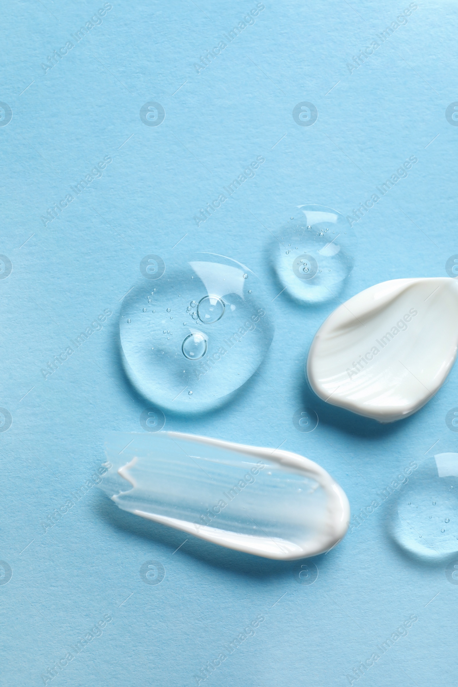 Photo of Samples of transparent gel and white cream on light blue background, flat lay