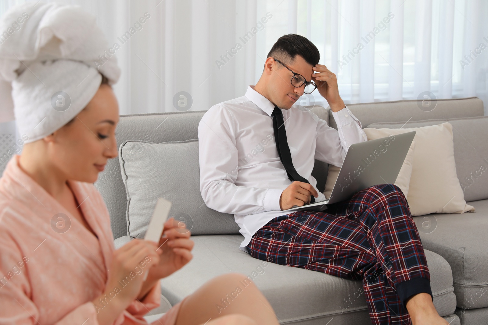 Photo of Man working on laptop while his wife relaxing in living room. Stay at home concept