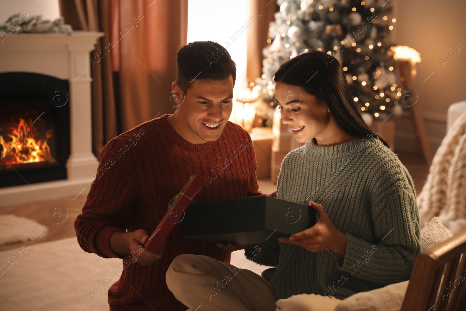 Photo of Couple opening gift box in living room with Christmas tree