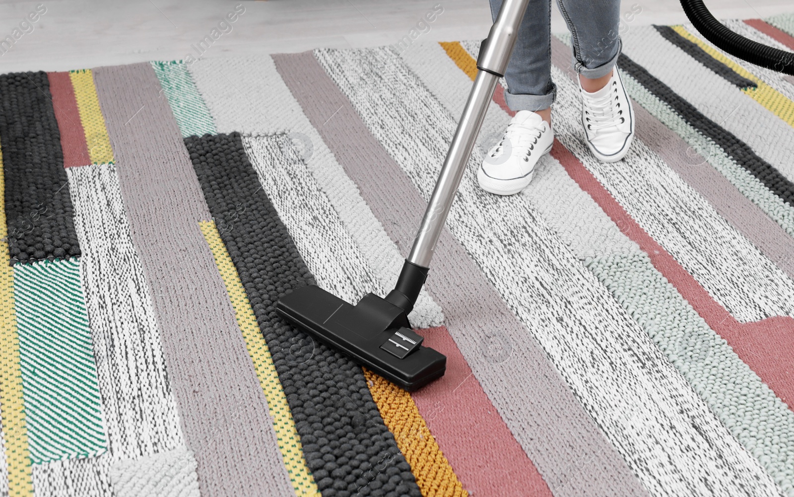 Photo of Woman removing dirt from carpet with vacuum cleaner at home