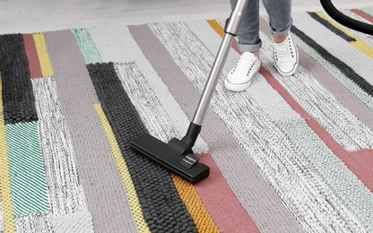 Woman removing dirt from carpet with vacuum cleaner at home