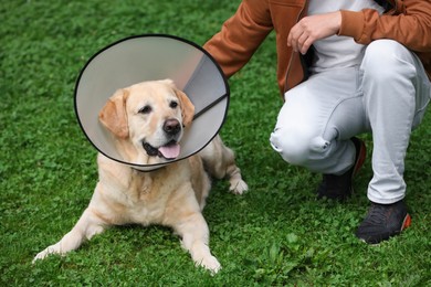 Man with adorable Labrador Retriever dog in Elizabethan collar on green grass outdoors, closeup