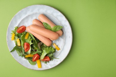 Photo of Delicious boiled sausages with salad on green, top view. Space for text