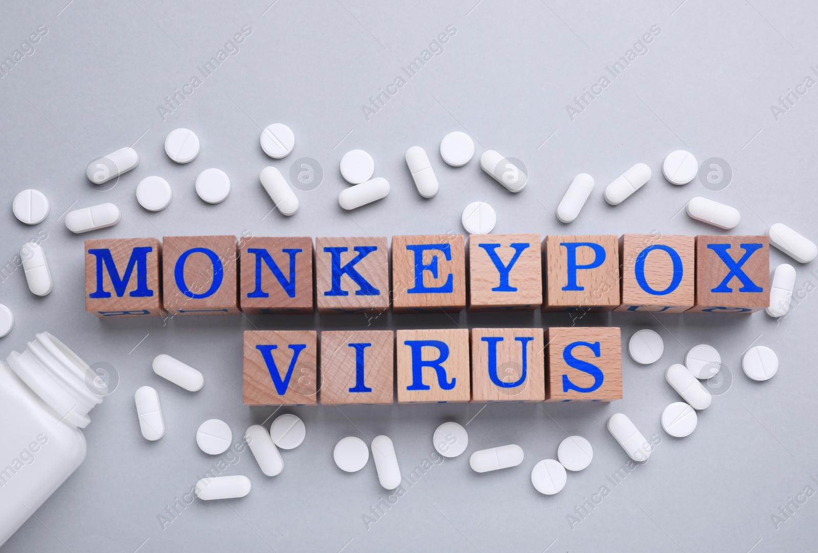 Photo of Words Monkeypox Virus made of wooden cubes and pills on light background, flat lay