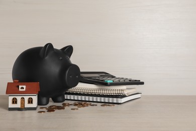 Piggy bank, house model, coins, calculator and notebooks on white wooden table. Space for text