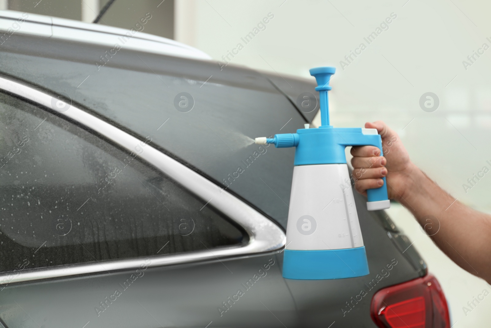 Photo of Worker spraying water onto car window before tinting in workshop, closeup