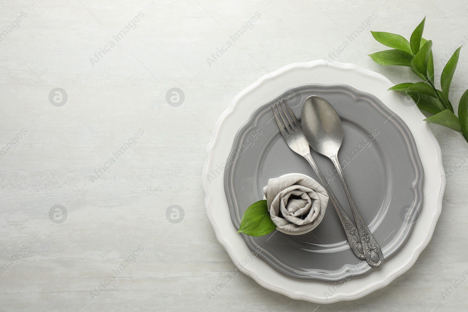 Photo of Stylish setting with cutlery, napkin, branch and plates on light textured table, top view. Space for text