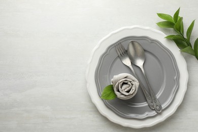 Stylish setting with cutlery, napkin, branch and plates on light textured table, top view. Space for text