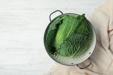 Colander with savoy cabbage and space for text on white wooden background, top view