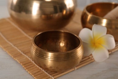 Golden singing bowl and plumeria flower on white wooden table, closeup