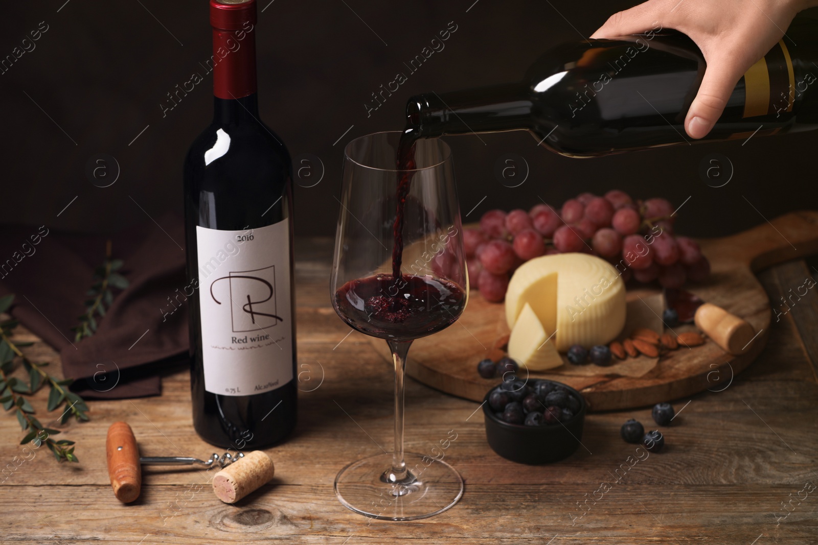 Photo of Woman pouring red wine into glass and appetizers on wooden table, closeup