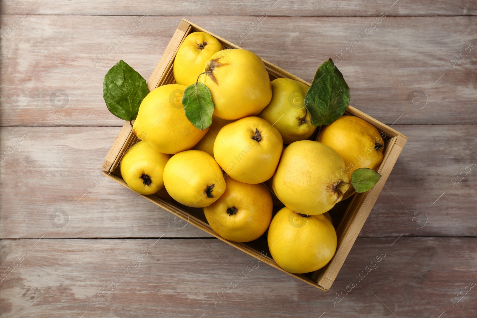 Photo of Tasty ripe quince fruits in crate on wooden table, top view
