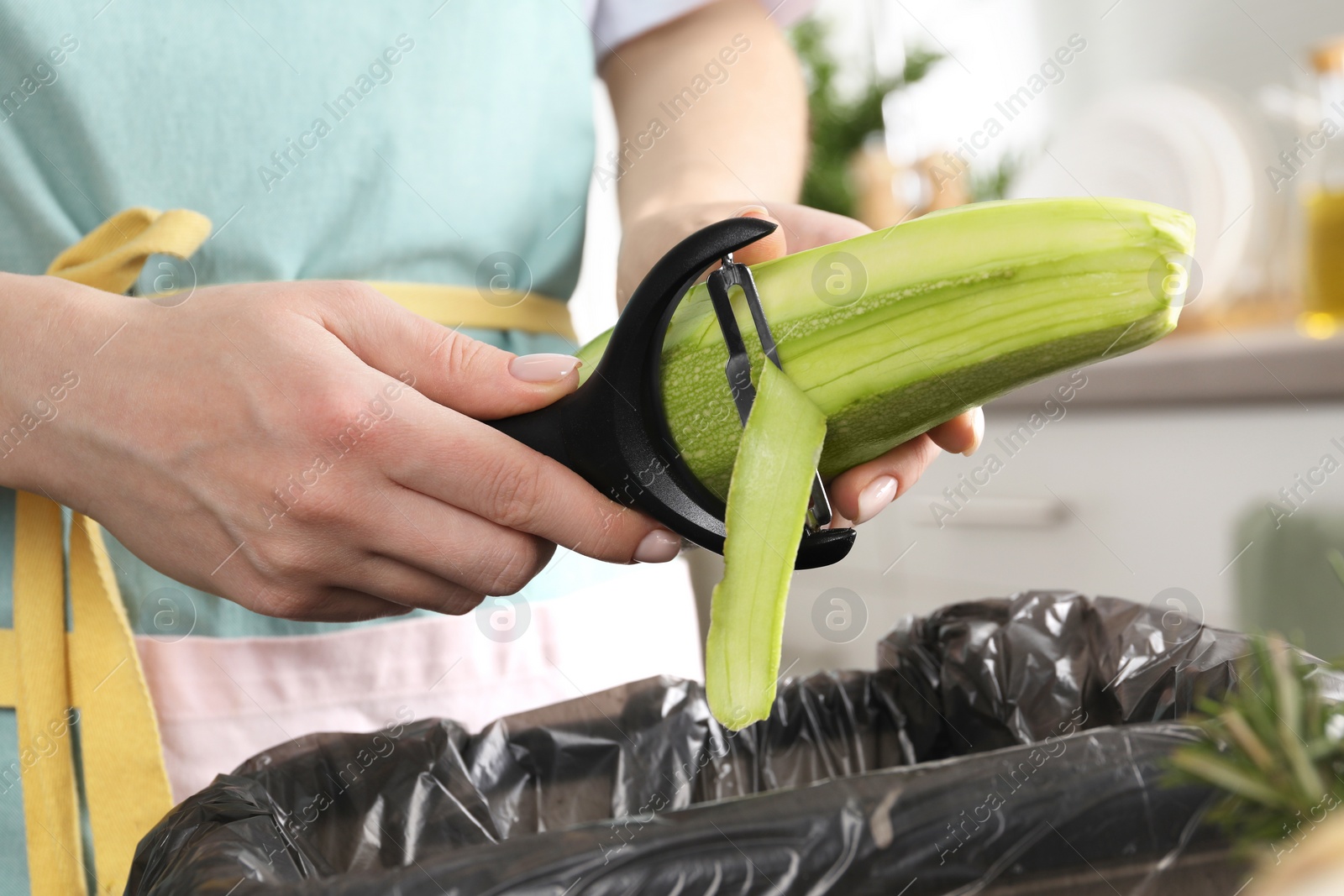 Photo of Woman peeling fresh zucchini above garbage bin indoors, closeup