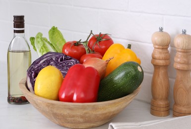 Wooden bowl with different raw vegetables on white countertop in kitchen