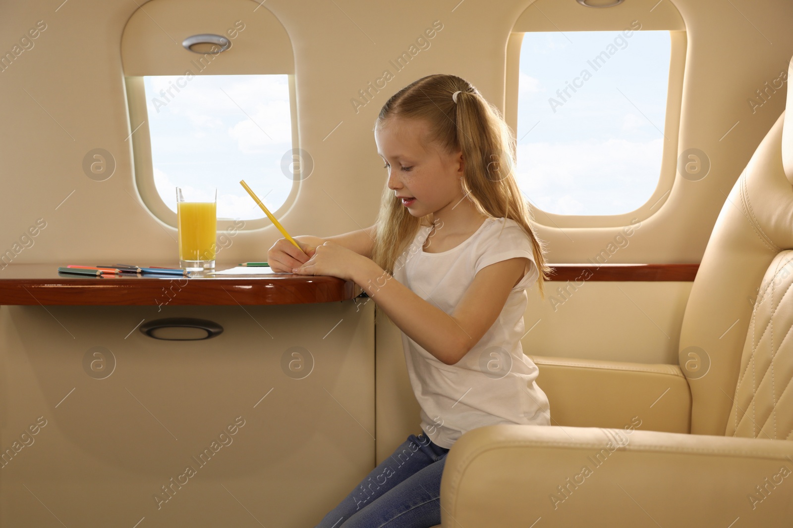 Photo of Cute little girl drawing at table in airplane during flight