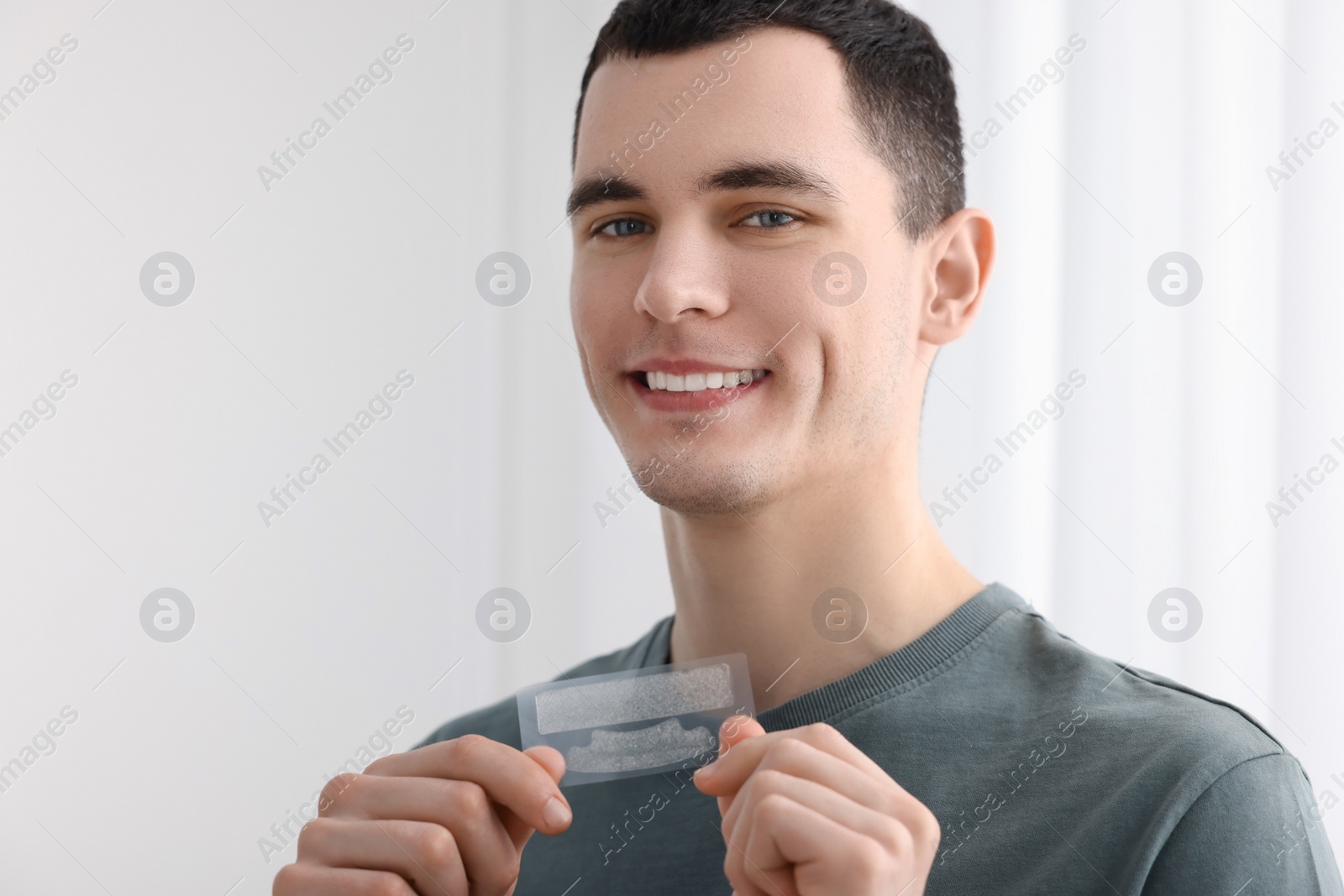 Photo of Young man with whitening strips on light background