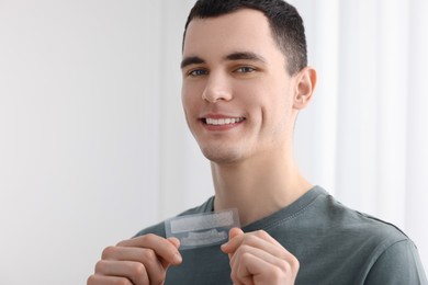 Young man with whitening strips on light background