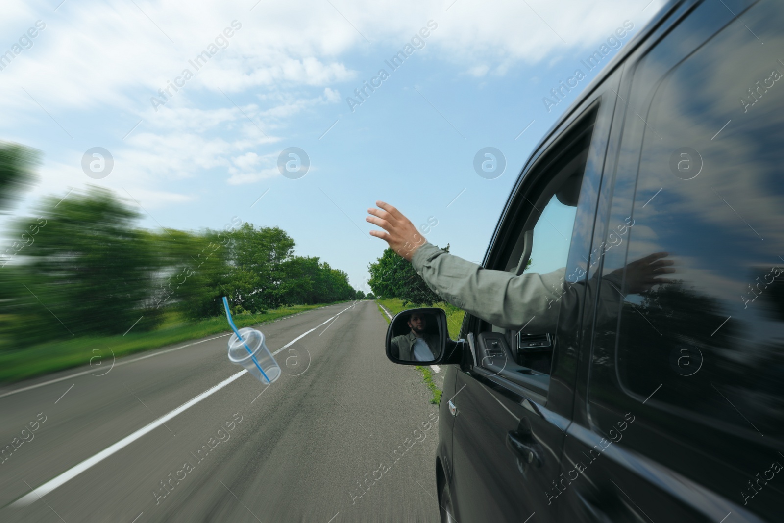 Photo of Driver throwing away plastic cup from car window. Garbage on road