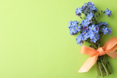 Photo of Beautiful blue forget-me-not flowers tied with ribbon on light green background, top view. Space for text