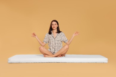 Photo of Young woman meditating on soft mattress against beige background