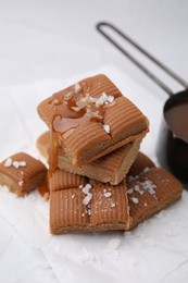 Yummy caramel candies, sauce and sea salt on white table, closeup