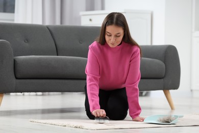 Photo of Woman with brush removing pet hair from carpet at home