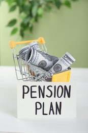 Photo of Card with phrase Pension Plan and dollar banknotes in toy shopping cart on white wooden table. Retirement concept