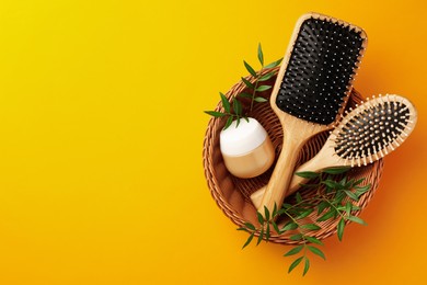 Photo of Wooden hairbrushes, jar of cosmetic product and leaves on orange background, top view. Space for text