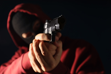 Man in mask holding gun on dark background, focus on hands
