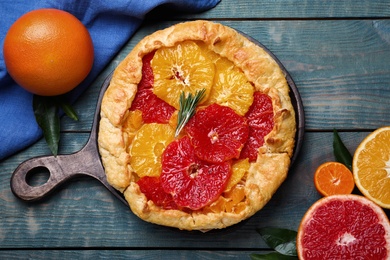 Photo of Delicious galette with citrus fruits and rosemary on blue wooden table, flat lay