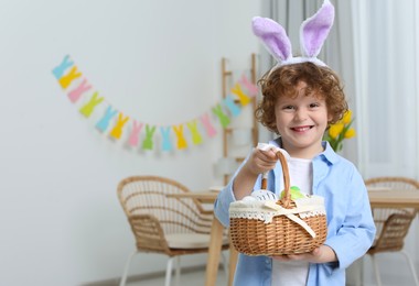 Photo of Happy boy in cute bunny ears headband holding Easter basket at home. Space for text