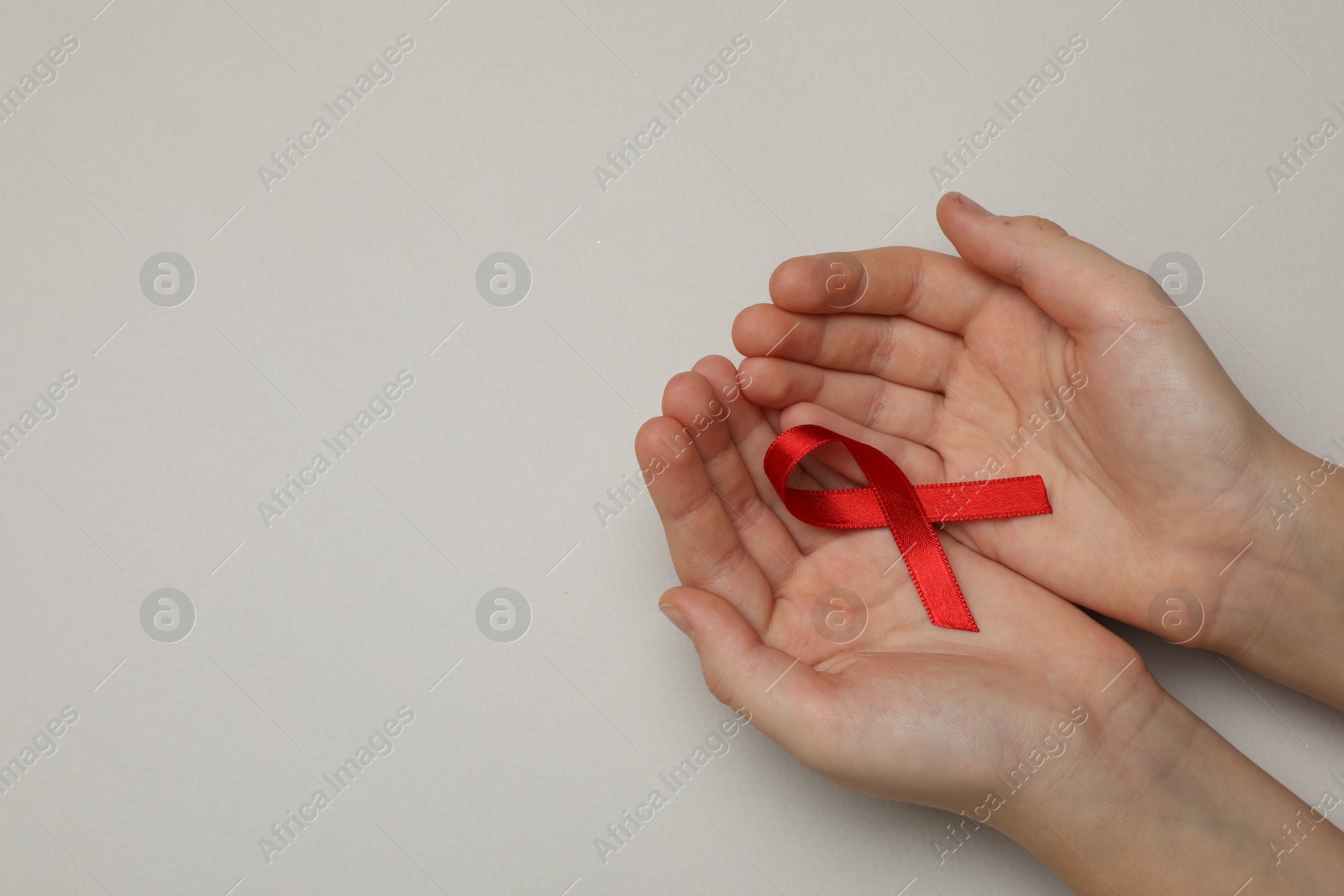 Photo of Little girl holding red ribbon on beige background, top view with space for text. AIDS disease awareness