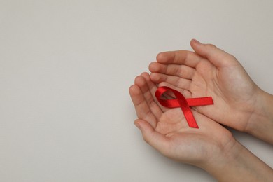 Little girl holding red ribbon on beige background, top view with space for text. AIDS disease awareness