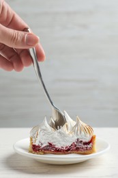 Photo of Woman eating delicious tartlet dessert with meringue and jam at white table, closeup