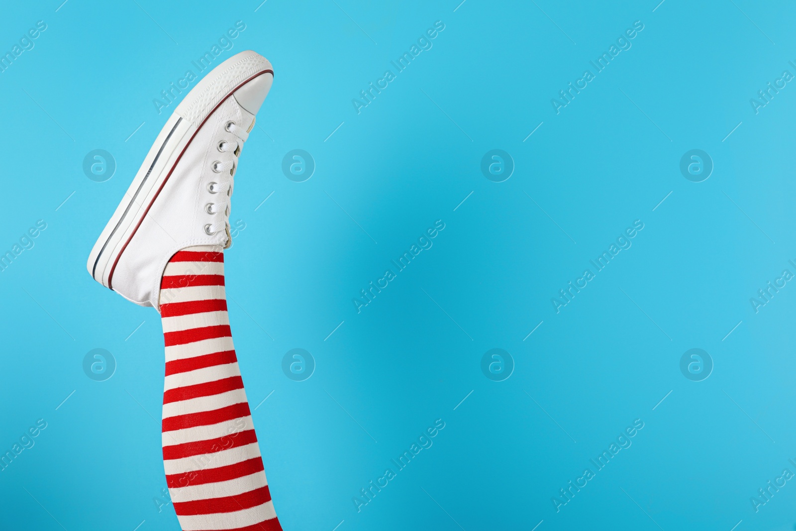 Photo of Woman wearing striped tights and sport shoes on light blue background, closeup. Space for text