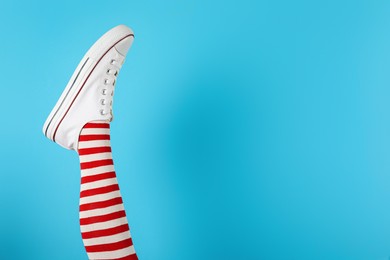 Woman wearing striped tights and sport shoes on light blue background, closeup. Space for text