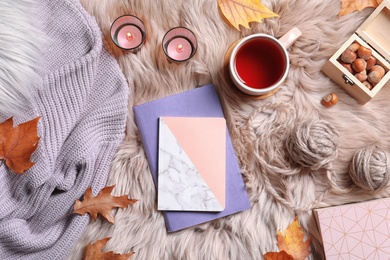 Photo of Flat lay composition with notebooks, cup of tea and warm clothes on fuzzy rug