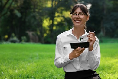 Photo of Lunch time. Happy businesswoman with container of food on green grass in park, space for text