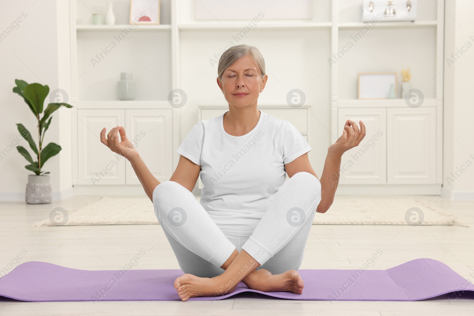 Photo of Senior woman practicing yoga on mat at home