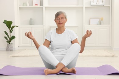 Photo of Senior woman practicing yoga on mat at home