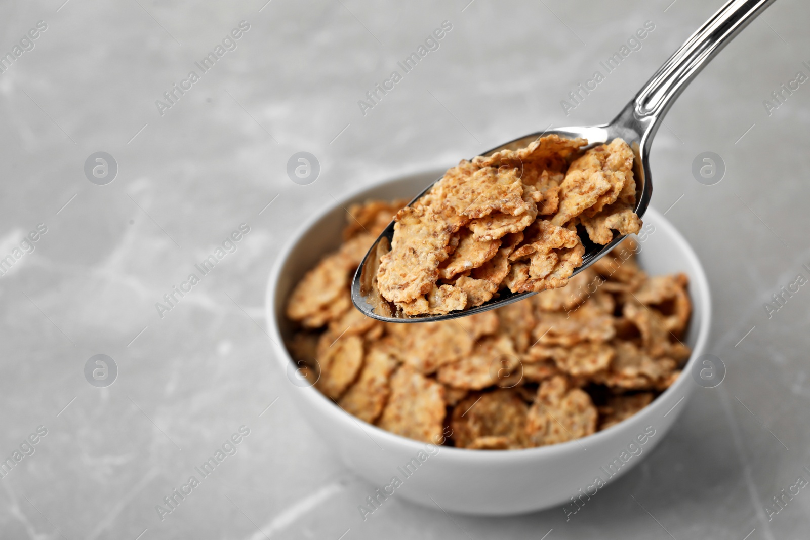 Photo of Spoon with cornflakes over bowl on table. Whole grain cereal