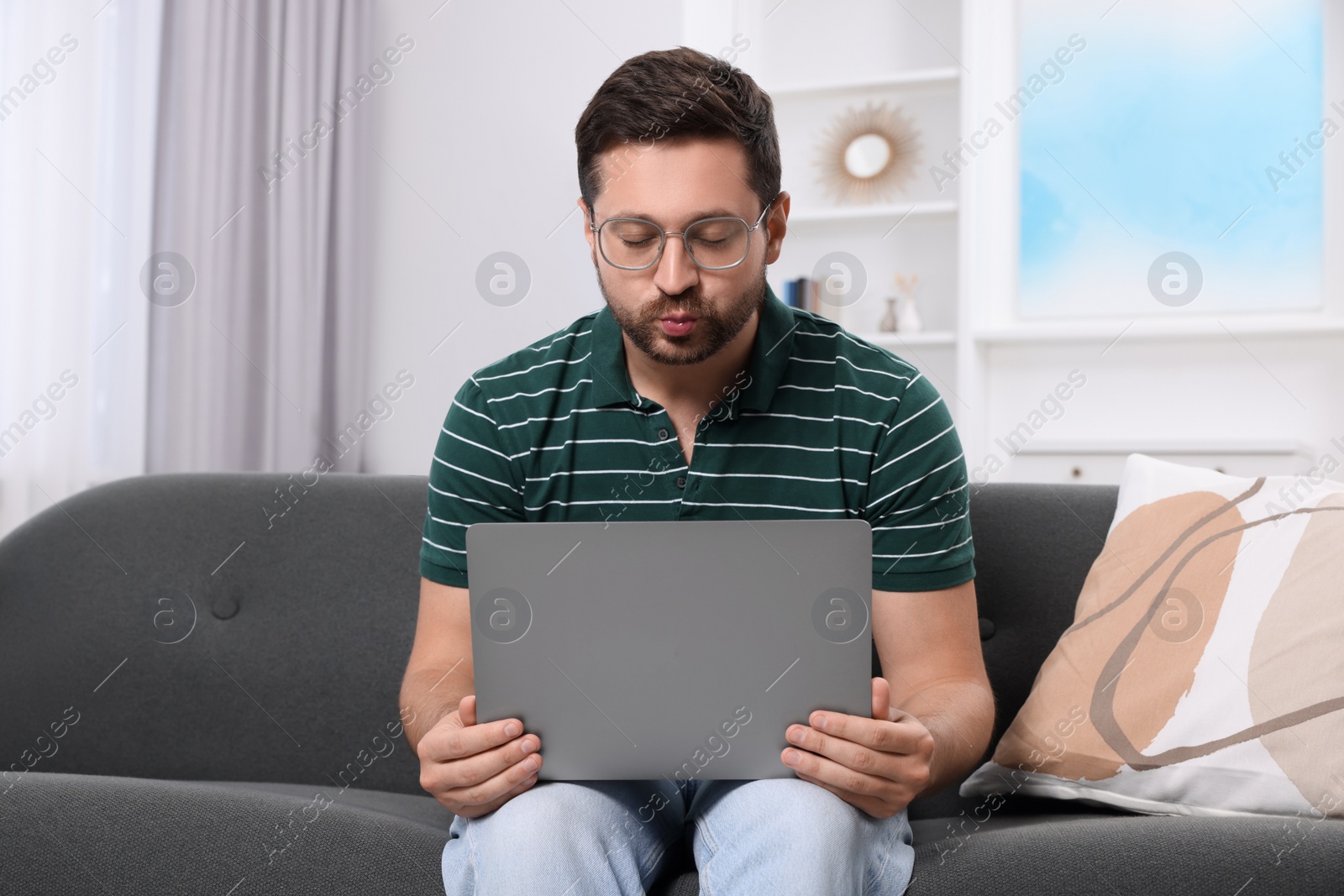 Photo of Man sending air kiss during video chat via laptop at home. Long-distance relationship