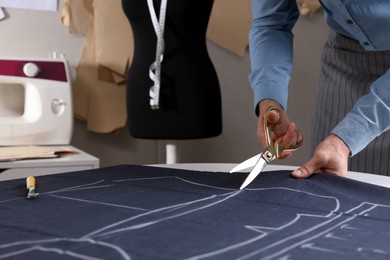 Photo of Tailor cutting fabric with scissors at table in atelier, closeup