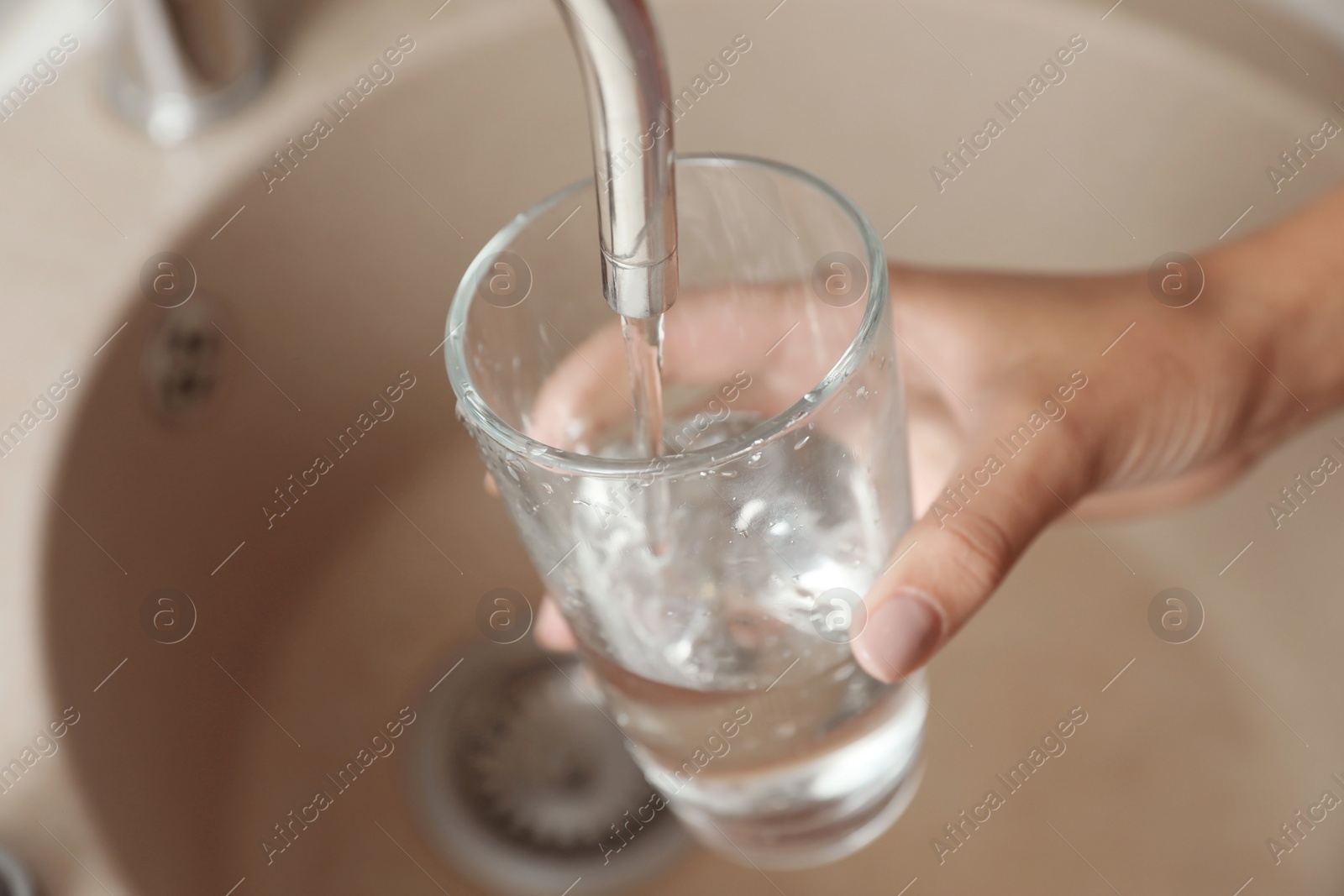 Photo of Woman pouring water into glass in kitchen, closeup