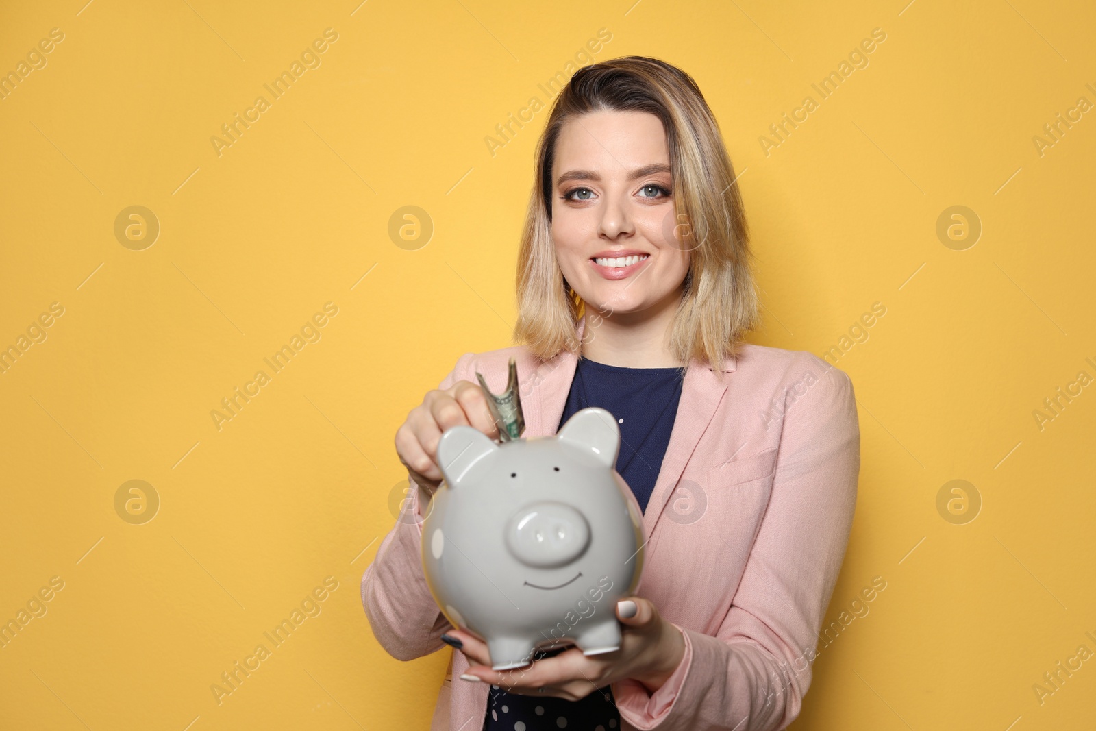 Photo of Beautiful businesswoman putting money into piggy bank on color background. Space for text