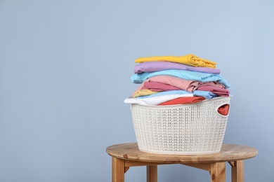 Photo of Plastic laundry basket with clean clothes on stool against color background. Space for text