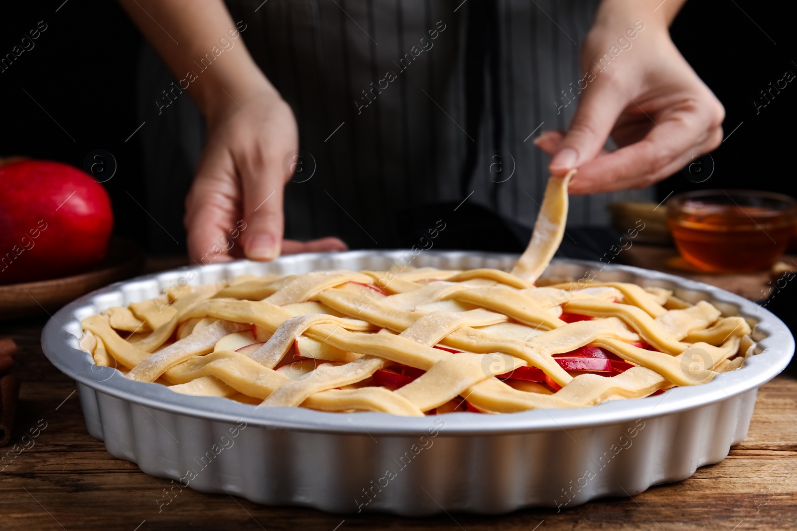 Photo of Woman making lattice top for traditional English apple pie at wooden table, closeup