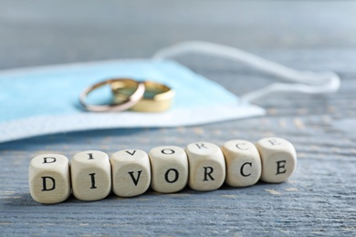 Photo of Cubes with word Divorce, protective mask and wedding rings on grey wooden table, closeup