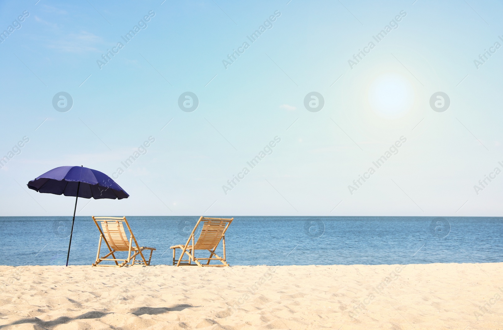 Photo of Empty wooden sunbeds and umbrella on sandy shore. Beach accessories